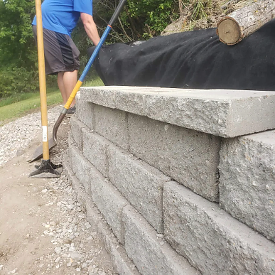A block retaining wall being built with cap stones going on over a compacted base